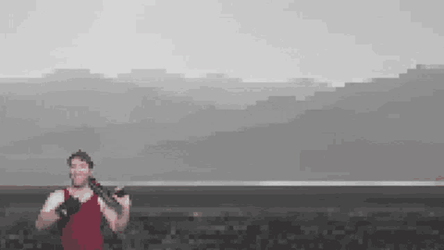 a man in a red tank top is holding a camera on a tripod