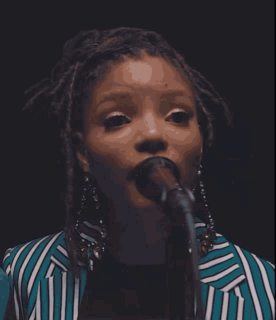 a woman singing into a microphone wearing a blue and white striped jacket