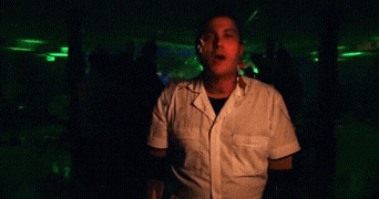 a man in a white shirt is dancing in a dark room while holding a microphone .