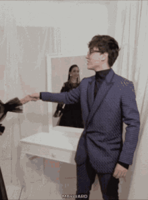 a man in a blue suit shakes hands with a woman in a black dress in front of a mirror