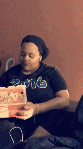 a woman wearing a shirt that says 2016 is holding a box of pizza