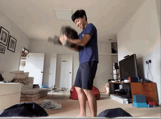a man in a blue shirt is standing in a living room holding a dumbbell
