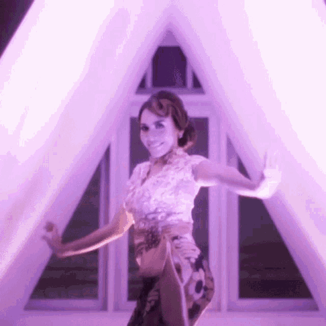 a woman is dancing in front of a window with purple lights