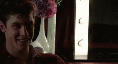 a young man is smiling in front of a mirror in a dark room with flowers in vases .