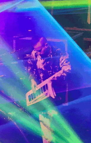 a man playing a keyboard with a rainbow of colors behind him