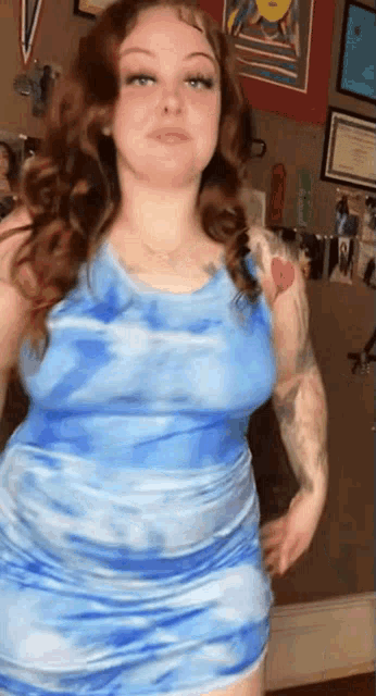a woman in a blue tie dye dress is standing in front of a wall .