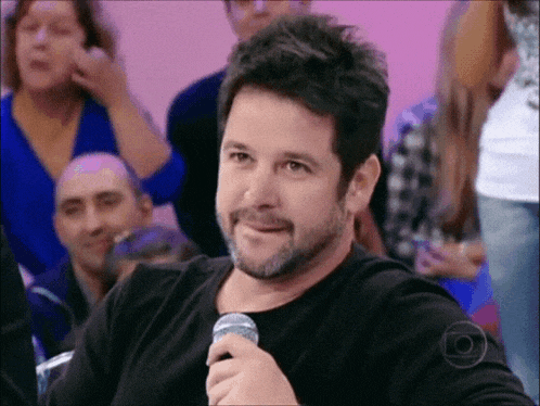 a man with a beard is smiling while holding a microphone in front of a crowd