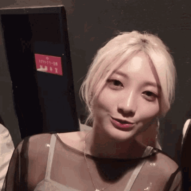 a woman with blonde hair is standing in front of a sign that says ' emergency exit '