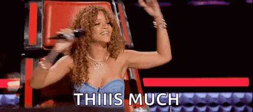 a woman is sitting in a chair with a microphone in her hand and says `` this is much '' .