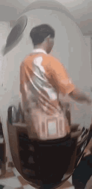 a man in an orange shirt is standing in front of a mirror looking at himself .