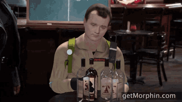 a man in a ghostbusters costume sits at a table with bottles of liquor