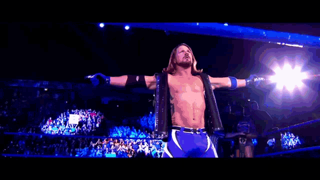 a wrestler is standing in a wrestling ring with his arms outstretched in front of a crowd .