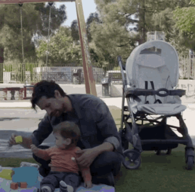 a man kneeling next to a baby and a stroller