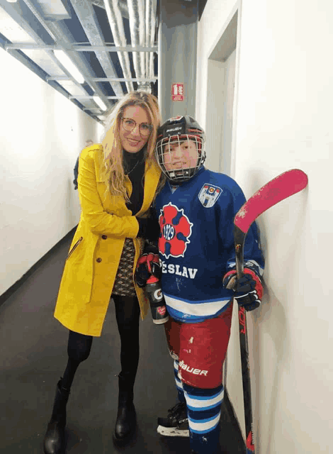 a woman stands next to a young hockey player wearing a jersey that says ' teslav ' on it