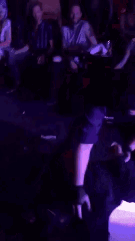 a group of people are sitting at tables in a dark room with purple lights behind them