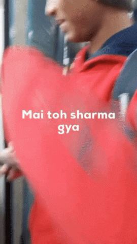a man in a red jacket is holding a red object and the words mai toh sharma gya are on the screen