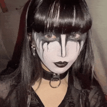 a woman with black hair and black makeup is wearing a choker and earrings .