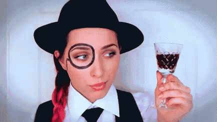 a woman wearing a hat and glasses is holding a glass of wine