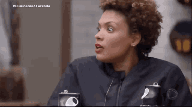 a woman with a surprised look on her face is sitting at a table with cups on it .