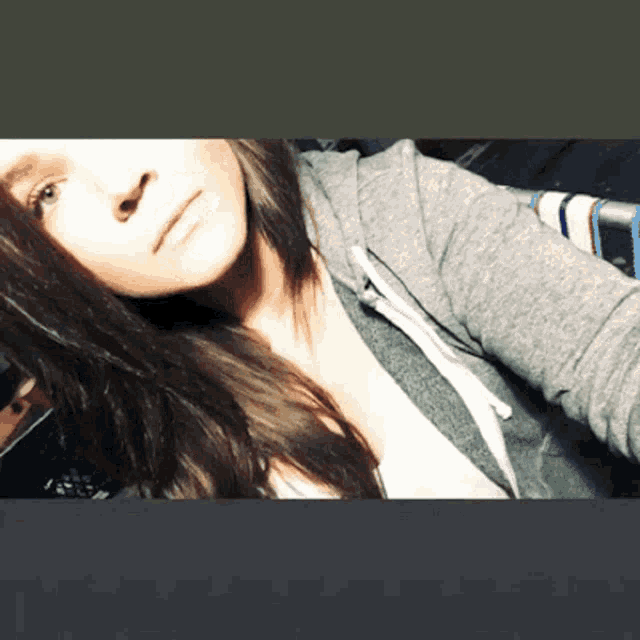 a woman with long dark hair is wearing a gray hoodie