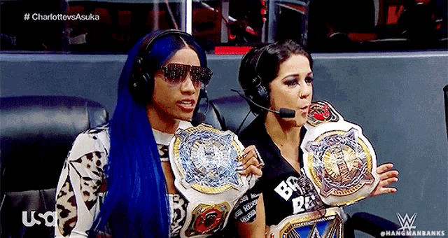 two women wearing headphones and holding wrestling championship belts