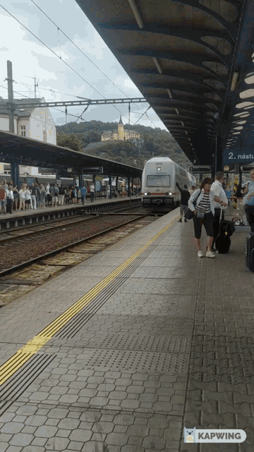 people waiting for a train at a train station with a sign that says kapwing