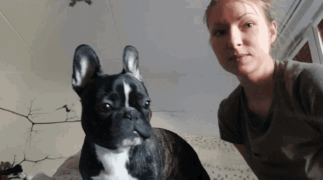 a woman stands next to a black and white dog looking at the camera
