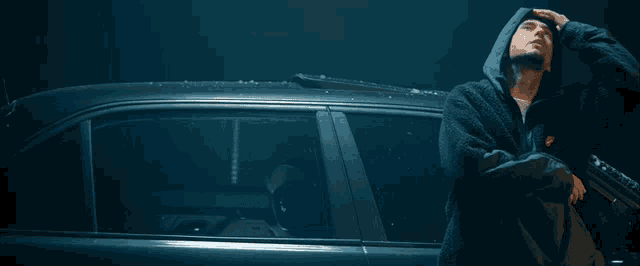 a man in a hooded robe stands next to a car