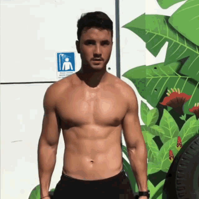 a shirtless man is standing in front of a wall with a sign on it that says ' no smoking ' on it