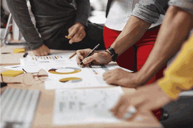 a group of people are sitting around a table looking at graphs