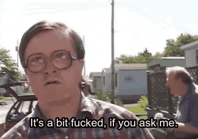a man wearing glasses and a plaid shirt is standing in front of a car and talking to another man .