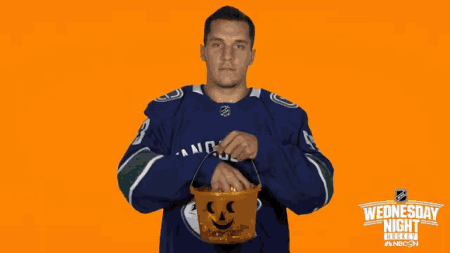 a man in a hockey uniform is holding a pumpkin and says " hallow "