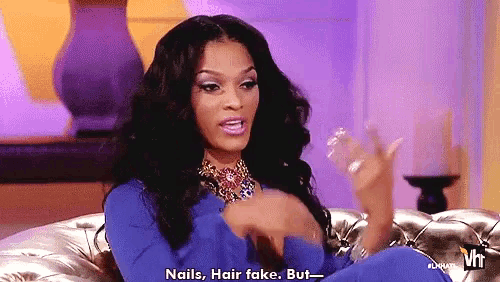 a woman is sitting on a couch and talking about nails , hair fake .