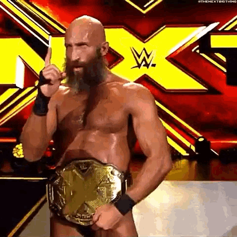 a man with a beard is wearing a wrestling belt and giving a middle finger .