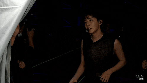 a man without a shirt is standing next to another man in a black vest .