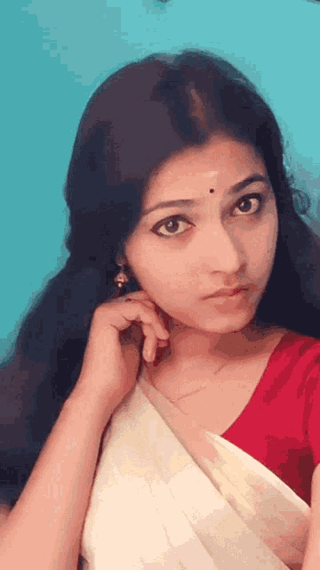 a woman wearing a red top and a white saree is looking at the camera