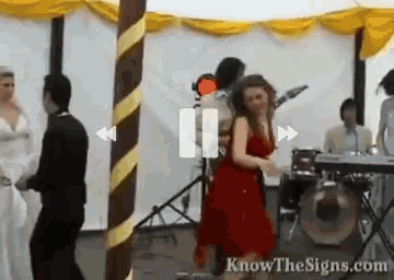 a woman in a red dress is dancing in front of a band with the website knowthesigns.com written on the bottom