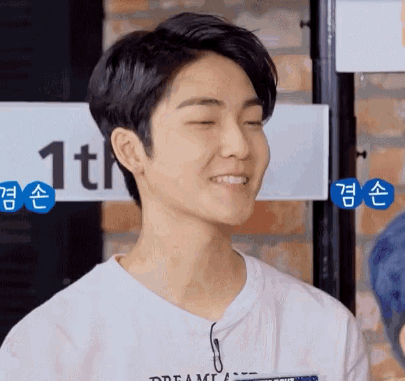 a young man wearing a white t-shirt with the word dream on it smiles with his eyes closed .