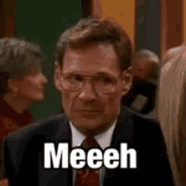 a man in a suit and tie is standing in front of a crowd and says meech .