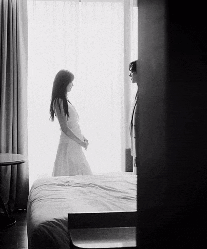 a woman in a white dress is standing in front of a window