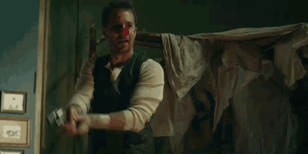 a man with blood on his face is standing in a dark room with his arms outstretched