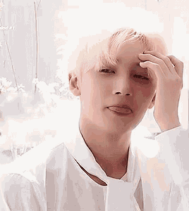 a young man in a white shirt and tie is touching his forehead with his hand .