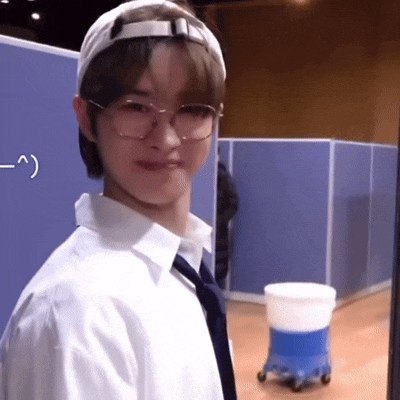 a man wearing glasses and a hat is standing in front of a blue cubicle