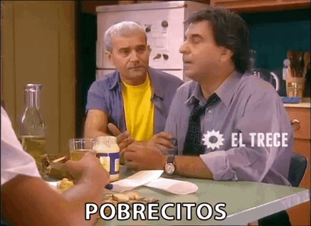 two men are sitting at a table in a kitchen and one of them is saying pobrecitos .