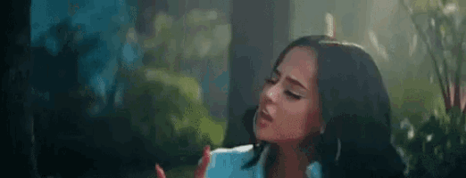 a woman is singing into a microphone in a forest while wearing a white shirt and earrings .