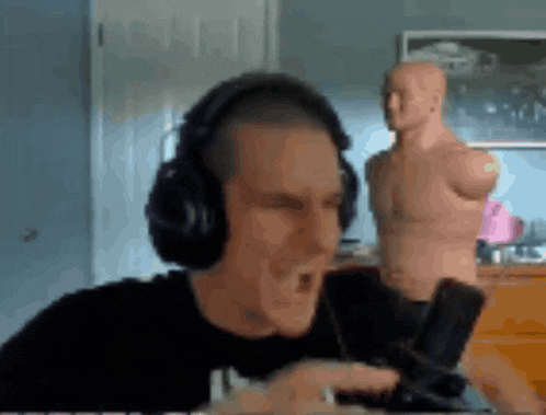 a man wearing headphones is singing into a microphone while a mannequin stands in the background .