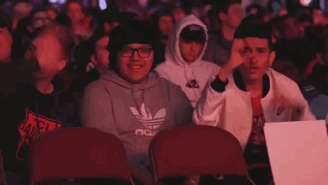 a man wearing a grey adidas hoodie sits in a crowd