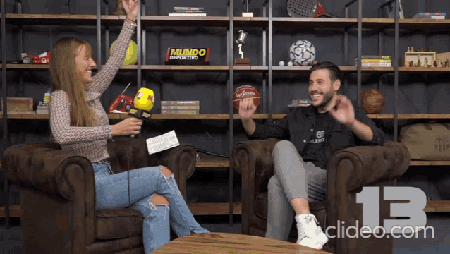a man and a woman are sitting in chairs in front of a shelf that says mundo deportivo on it