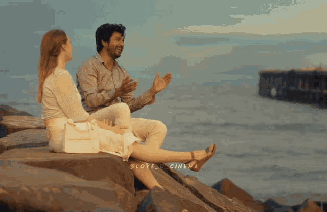 a man and a woman are sitting on rocks near the ocean and the words love cinema are visible on the bottom
