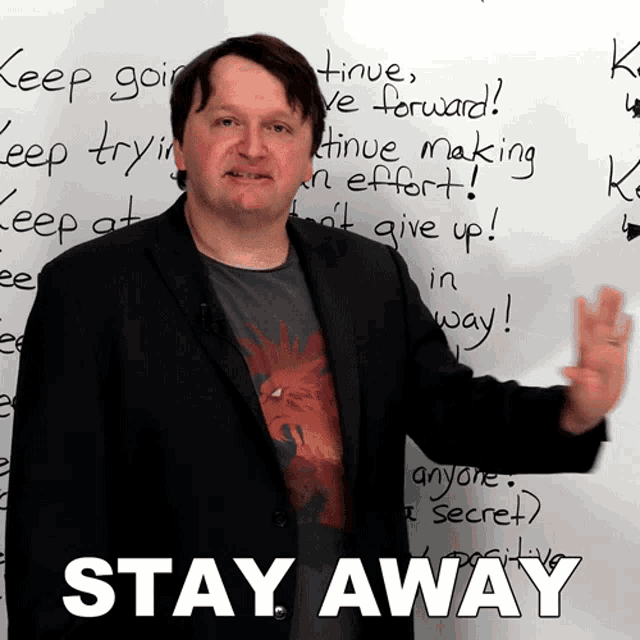 a man in a suit stands in front of a white board that says stay away